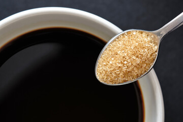 Top view, Close up of teaspoon of brown sugar, cane sugar with white cup of coffee, copy space for text.