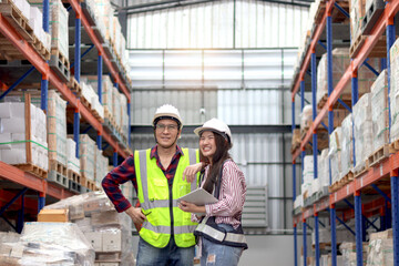 Fototapeta na wymiar Happy Young Asian woman and senior man worker wearing safety vest and helmet, working at factory warehouse. Father and daughter work together in storage of family business.