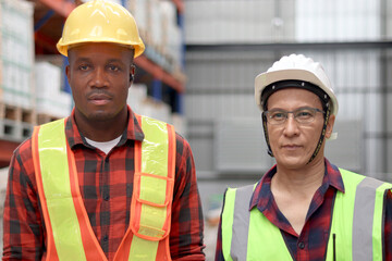 Portrait of African worker and Asian senior supervisor wearing safety vest and helmet, standing at...