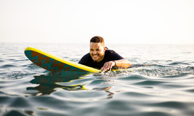 A dark-skinned man is surfing dressed in a neoprene. The African is paddling with his hands on the surfboard. Surfing concept. Black men doing water sports.