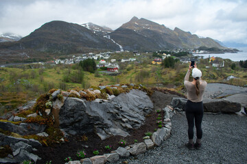 Fototapeta na wymiar Reine, Lofoten, Norway. Female tourist taking scenic picture of the island from nearby hill