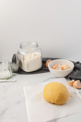 Ball of Homemade Pasta Dough on Marble Countertop with Ingredients in Background