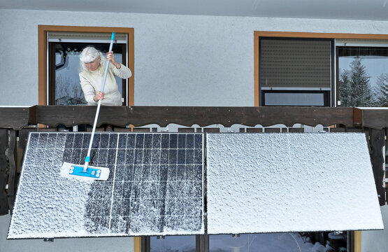 Eine Frau befreit im Winter ein Balkonkraftwerk vom Schnee