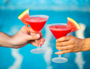 People hold watermelon cocktail near pool