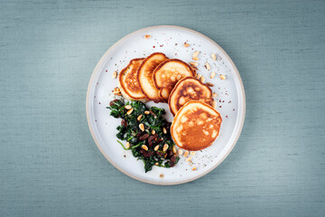 Traditional American pancakes with spinach, pine-nuts and raisins served as top view on a Nordic...