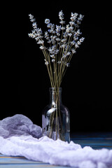 Glass bottle with dry lavender branches on a dark background