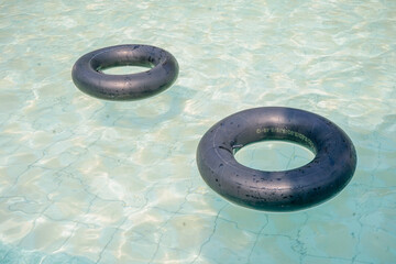Two black inflatable rings floating peacefully in the crystal clear water of a swimming pool on a bright, sunny day, evoking a sense of summer vacation and relaxation.