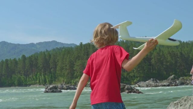 Cute Boy Is Throwing Handmade Glider Outdoors. Slow motion. Happy little boy launch model airplane into the sky. Happy carefree childhood. Toy plane against blue sky. Boy playing with toy aircraft.