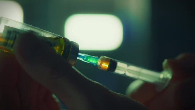 An addicted person taking drugs prepares a dose of a narcotic substance by filling a syringe with a bright liquid. Taking drugs of narcotic origin intravenously using a needle and syringe