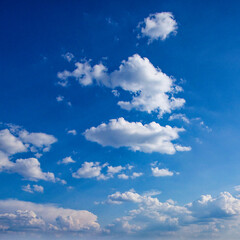 The image shows a bright blue sky with scattered white clouds. The clouds are fluffy and vary in size, floating under the sunlight.