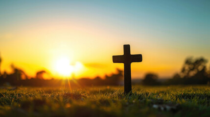 Silhouette cross at sunrise on grass.