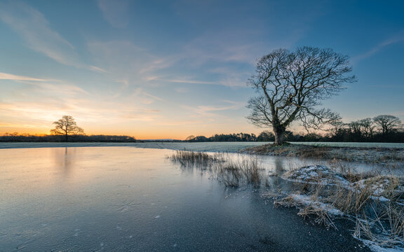 Winter sunrise in nature with frozen pond and orange and blue sky