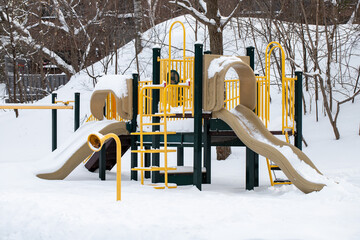 Playground with slides in park, covered with snow in winter