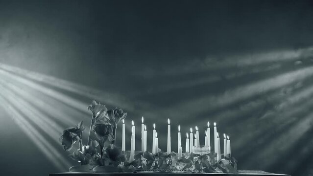 Monochrome background, rays of light fixtures illuminate the festive table. There are candles burning on the table and fresh flowers. Depressive holiday and disappointment concept.