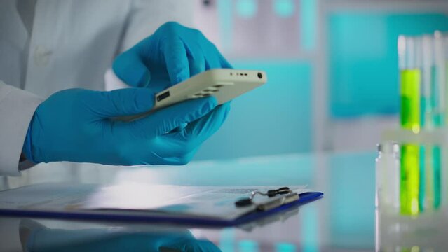 Vaccine. Scientist doctor in protective suit carefully uses modern smartphone in modern laboratory. Cinematic shot of young expert looking at phone screen creating cures for diseases, biotechnology