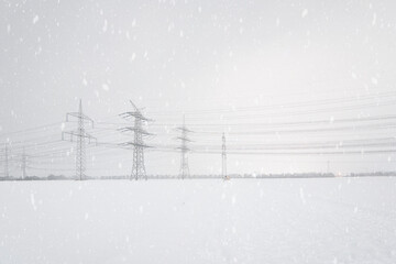 A lot of high-voltage power line in winter with lots of snow on the fields, electrical energy transmission tower overhead line masts, high voltage pylons as power pylons on the fields in winter 