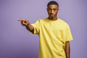 African American man in yellow shirt pointing on purple background.