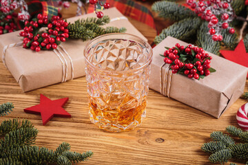 Glass of whiskey or bourbon with festive Christmas decoration on light wooden background. New Year,...
