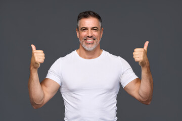 Happy fit sporty older man coach, middle aged personal trainer wearing white t-shirt showing like thumbs up standing isolated on gray background motivating for good results giving recommendation.