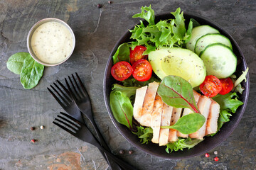 Healthy homemade salad bowl with avocado and chicken. Above view table scene on a dark slate stone background.