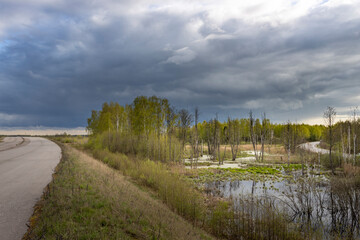 spring landscape with a cloudy sky and a highway,Abandoned highway, spoiled nature, swampy roadside area, environmental damage due to the construction of the highway.