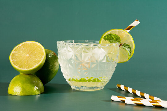 Caipirinha glass of Pinga Cocktail with Ice and Lime on a Smooth Green Background with lemon basket in front photo