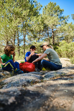 Focused family members eating while sitting on rocky terrain in forest