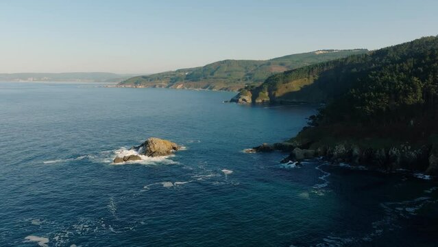 Drone footage over the Ocean of Malpica with green mountins and splashing waves in Spain
