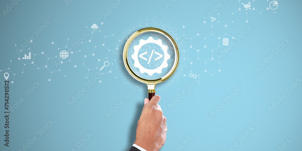 Wall mural web development: businessman hand holding a magnifying glass with coding icon on light blue backgrou