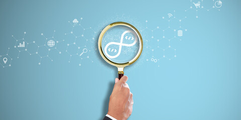 DEVOPS: Businessman Hand holding a magnifying glass with DevOps icon on Light Blue background....