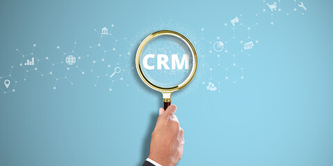 CRM. Businessman Hand Holding a Magnifying Glass with Customer Relationship Management Icon on Light Blue Background. Database Analysis, Customer Engagement.