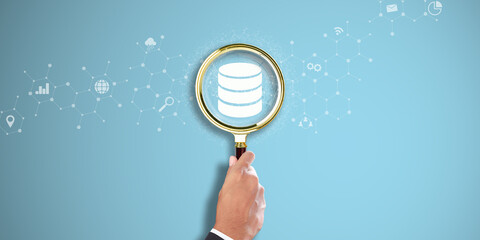 Database Management: Businessman Hand Holding a Magnifying Glass with Database Icon on Light Blue...