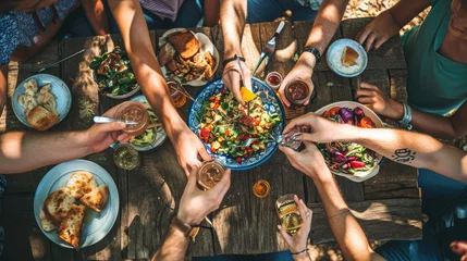 Muurstickers Top view of a group of people sitting around a rustic wooden dining table, toasting with their glasses raised amidst a spread of various dishes © MP Studio