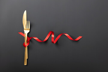 Fork and knife tied with a red ribbon on black background. Romantic dinner. Valentine's Day
