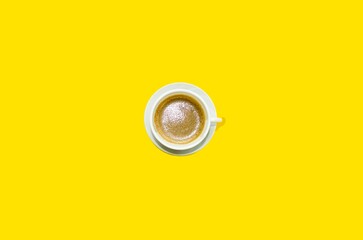 On a bright yellow background in the center there is a white cup with black coffee, cappuccino.  Space for copy text, flat lay.  Fragrant, delicious hot coffee.  Top view, close-up.