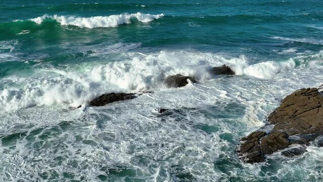 Slow Motion of Bubbling Blue Ocean Water breaking rocks with White Foam on a sunny day