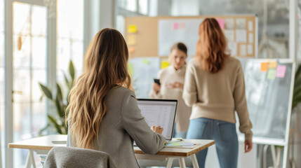 Colleagues in a modern office setting, one from behind, working at a computer.
