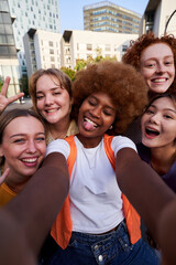 Happy multiracial group of female friends taking a funny selfie with a smartphone. Cheerful young women gathering together using phone to take photos looking at camera. Vertical social media image.