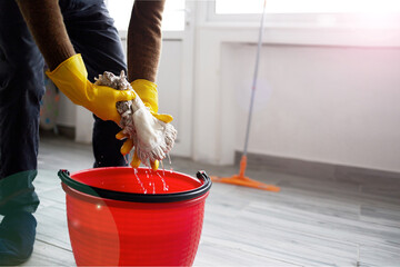 Hands in rubber gloves wring out a mop over a bucket. The concept of cleanliness and health care.
