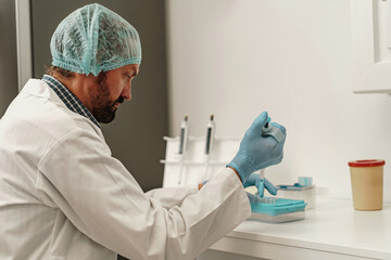 Male scientist in uniform is using micropipette for biochemical test analysis in medical laboratory