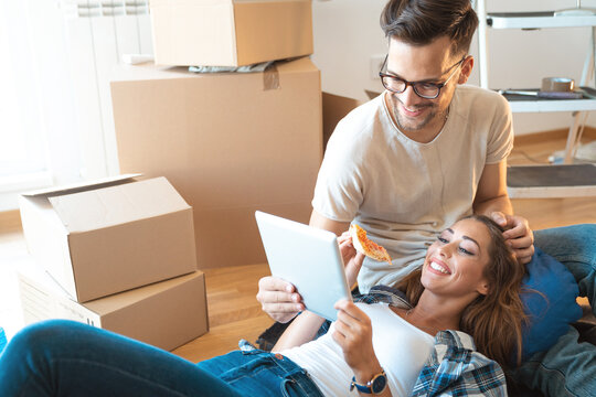Young smiling couple surfing the net and looking for some home decoration ideas online in new apartment. Young couple in love using digital tablet pc shopping online in new family home. - Powered by Adobe