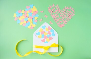 Paper craft for Valentine's Day.  On a green background there is an applique of colored paper hearts and heart-shaped butterflies flying out of an envelope.  Handmade concept, Valentine's Day holiday.