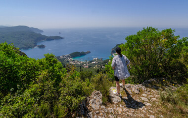 Traveler hiker girl enjoying landscape of Palaiokastritsa in Corfu, Greece from a mountain top during hot summer day