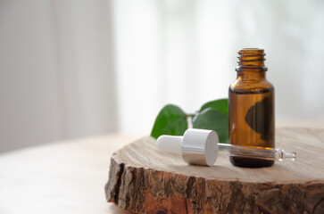 Glass dropper bottle on a wooden podium on a white background with shadows, leaves. Cosmetic...
