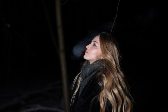Young blond Woman with black dress in the wood at an snowstorm in deep winter at berlin forrest