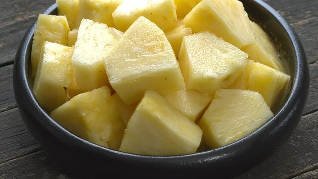 Pineapple chunks in a bowl on a rustic wooden table. Table spin. 
