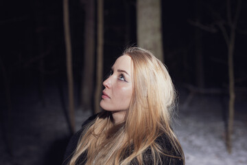 Fototapeta premium Young blond Woman with black dress in the wood at an snowstorm in deep winter at berlin forrest