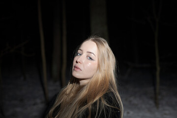 Fototapeta premium Young blond Woman with black dress in the wood at an snowstorm in deep winter at berlin forrest