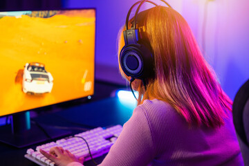 Young player woman wearing gaming headphones intend to do playing live stream games online at home, Happy Gamer endeavor plays online video games tournament with computer with neon lights, Back view - obrazy, fototapety, plakaty