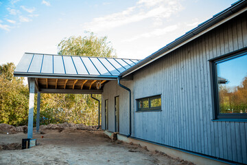 Modern wooden house under construction with blue siding and exposed roof framework on a sunny day